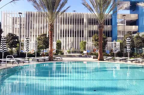 Resort courtyard with turquoise swimming pool, palm trees, and modern striped building facade
