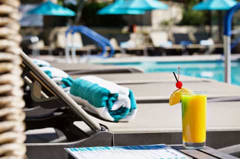 Poolside cocktail with cherry garnish on lounge chair beside turquoise swimming pool