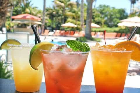 Three colorful tropical cocktails with citrus garnishes poolside at resort