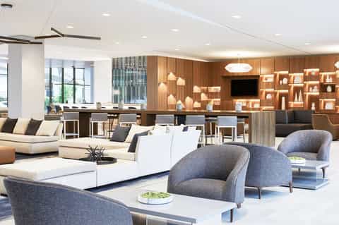 Modern hotel lobby with contemporary furniture, wooden shelving, and bar seating area