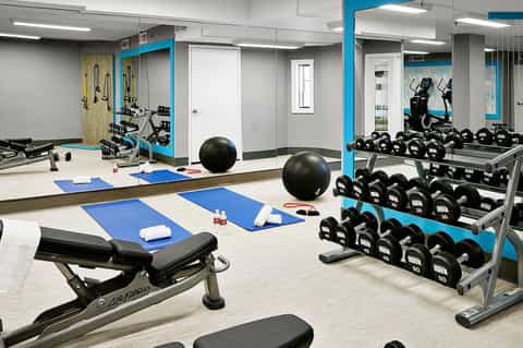 Modern fitness studio with blue accents, dumbbells, exercise bikes, stability balls, and mirrored walls