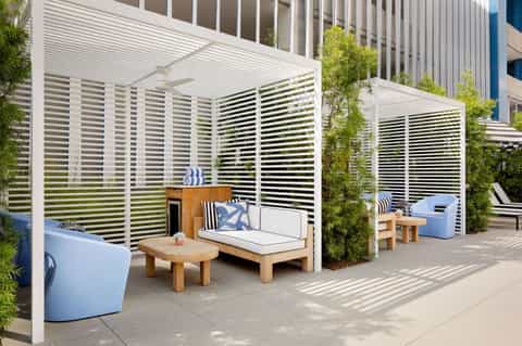 Modern lounge seating area with white pergola, striped privacy screens, and wood furniture