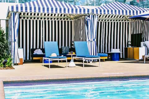 Striped cabanas and lounge chairs beside a sparkling swimming pool