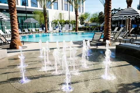 Modern resort pool with illuminated fountains, palm trees, and striped umbrellas
