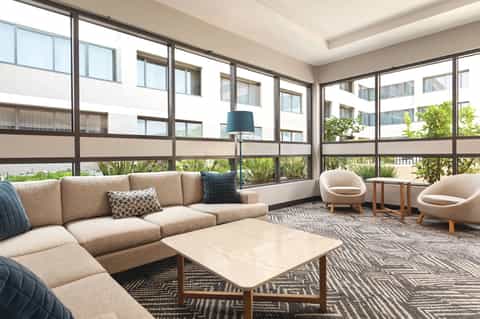 Modern resort lounge with beige sectional sofa, floor-to-ceiling windows, and garden views
