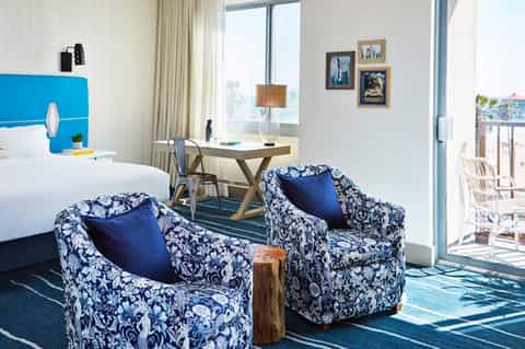 Modern hotel room with blue accent headboard, patterned chairs, and ocean view from private balcony