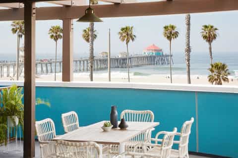 Beachfront dining area with white chairs, turquoise pool wall, and ocean pier views