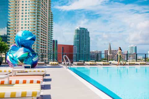 Rooftop pool deck with colorful loungers, blue water, and high-rise city skyline backdrop