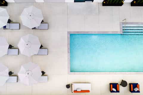 Aerial view of modern pool with white umbrellas, lounge chairs, and spa area