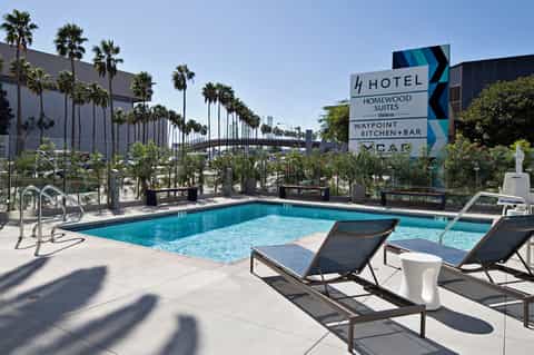 Resort pool area with lounge chairs, palm trees, and hotel sign for Homewood Suites