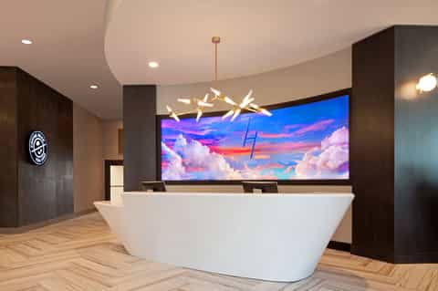 Modern hotel lobby with curved white reception desk and colorful sky artwork