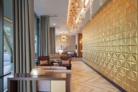 Modern hotel lobby with geometric wall patterns, hanging pendant lights, gray curtains, and contemporary seating areas