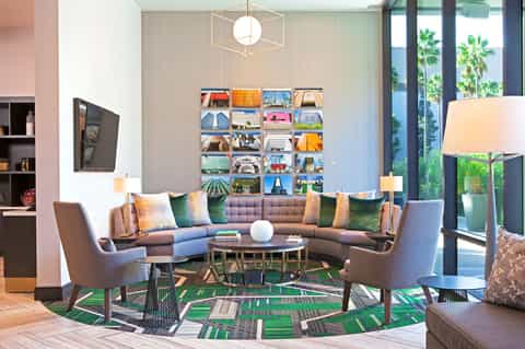 Modern hotel lobby with curved sectional sofa, colorful photo wall art, geometric rug, and floor-to-ceiling windows