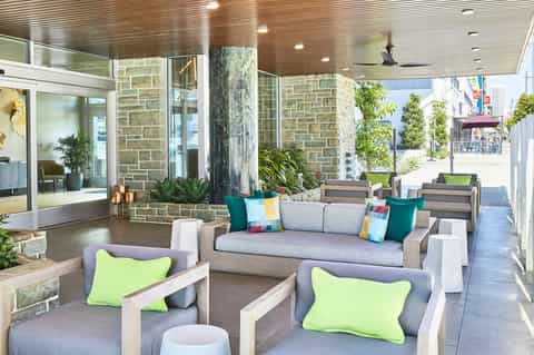 Modern covered patio lounge with stone columns, gray seating, colorful pillows, and mountain views