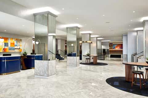 Modern hotel lobby with marble flooring, blue reception desk, and tall support columns