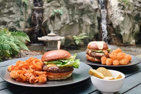 Gourmet burgers with crispy shrimp and fries served in a lush garden setting with stone features