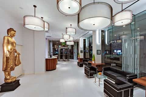 Modern hotel lobby with cylindrical pendant lights, gold Buddha statue, black seating, and glass partitions
