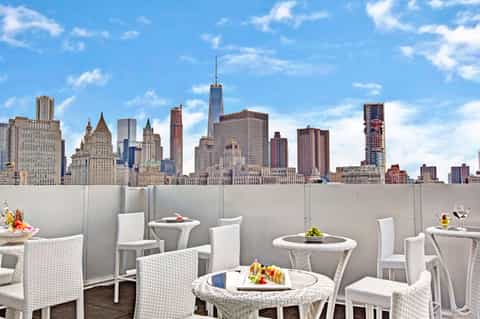 Rooftop dining area with white wicker furniture overlooking Manhattan skyline