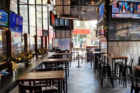 Modern bar interior with black furniture, multiple TV screens, holiday decorations, and street view