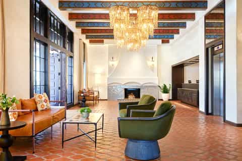 Luxury hotel lobby with ornate ceiling beams, crystal chandelier, orange leather sofa, fireplace, and Southwest design