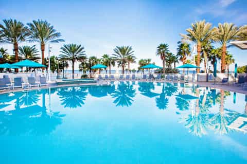 Resort pool with crystal blue water, palm trees, turquoise umbrellas, and beachfront loungers