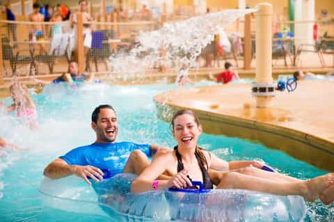 Families enjoying indoor water park with wave pool, water slide, and shallow play areas for children.