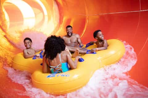 Children riding yellow water slide through pink foam splash at amusement park
