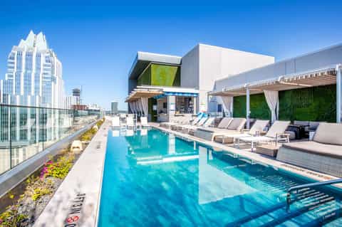 Modern rooftop pool with turquoise water, loungers, pergolas, and city skyline backdrop