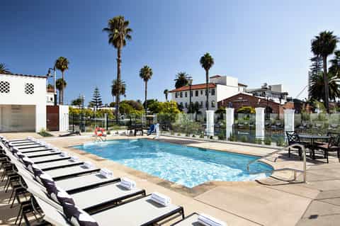 Resort pool with white loungers, palm trees, and Mediterranean-style architecture buildings