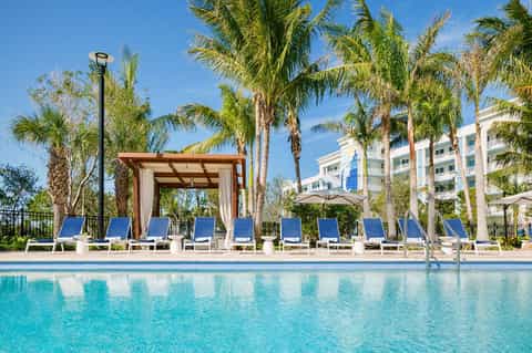 Luxury resort pool deck with palm trees, cabanas, and waterfront building
