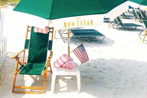 Beach chair under green umbrella with pink towel and American flag at The Don Cesar resort
