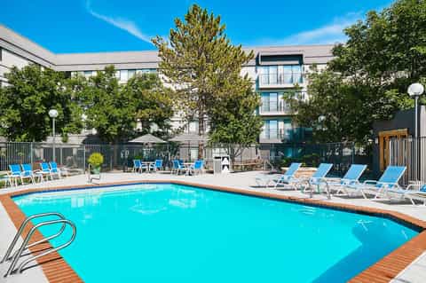 Modern hotel courtyard pool surrounded by blue lounge chairs, trees, and contemporary building with balconies