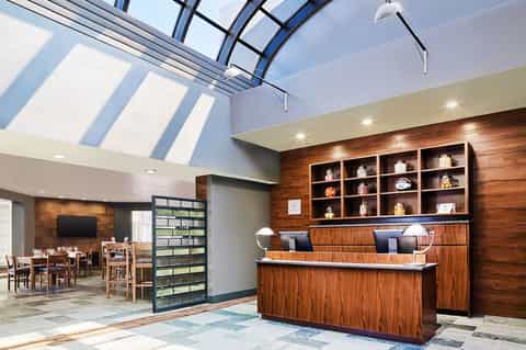 Modern hotel lobby featuring wooden accent wall, reception desk, and skylight ceiling with natural light