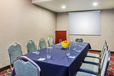 Conference room with blue-draped rectangular table, chairs, projector screen, and fruit centerpiece