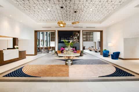 Spacious modern hotel lobby with geometric patterned ceiling, wooden accents, and circular striped floor design