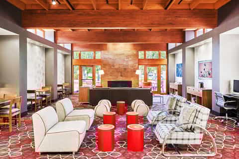 Modern hotel lobby with wood beamed ceiling, red accent chairs, fireplace, and contemporary furniture