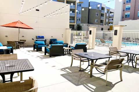 Outdoor patio with lounge seating, orange umbrella, string lights, and pool access