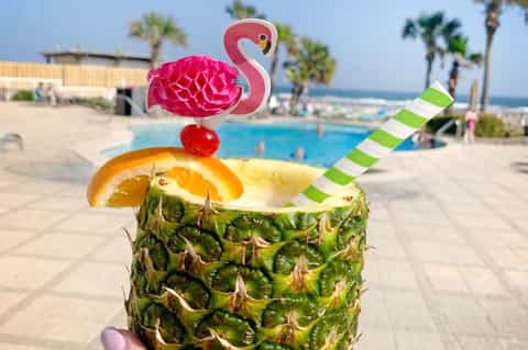 Tropical cocktail in pineapple with flamingo garnish by resort pool and ocean
