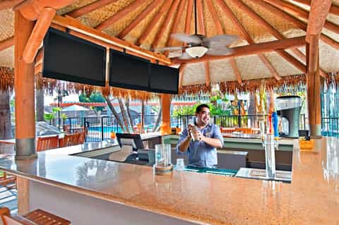 Bartender working at an outdoor tiki bar with ocean views and woven roof structure