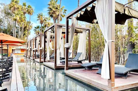Modern spa cabanas with white curtains and dark lounge chairs along a reflective water feature