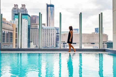 Woman in black dress standing by rooftop pool with city skyline and green pillars in background