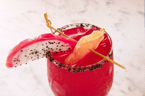 Vibrant red cocktail with dragon fruit garnish and gold straw on white background
