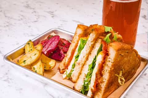 Gourmet sandwich with bacon, tomato, and lettuce served with potatoes and beverage