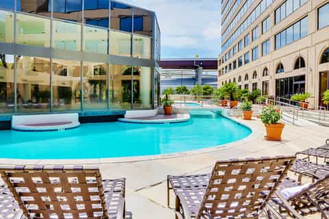 Modern curved hotel pool with lounge chairs, surrounded by contemporary glass and stone architecture