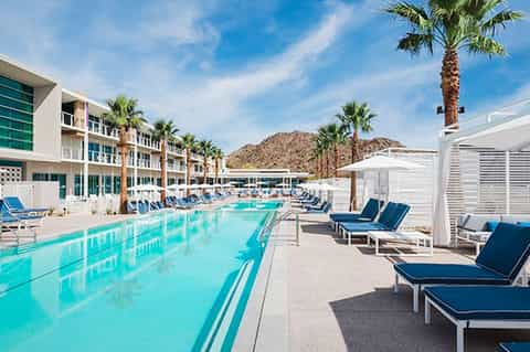 Resort pool deck with turquoise water, lounge chairs, palm trees, and desert mountain backdrop