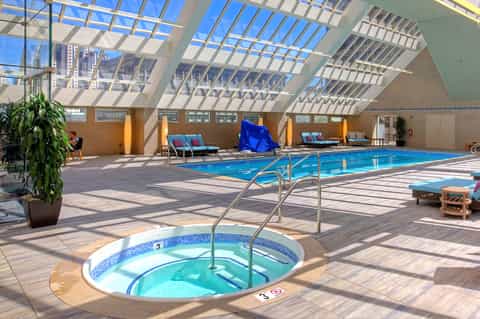 Indoor aquatic center with Olympic-sized pool, hot tub, and skylights casting geometric shadows on wood decking