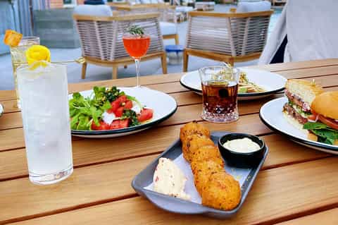 Beachfront dining table with salads, fried appetizers, cocktails, and refreshing beverages at sunset