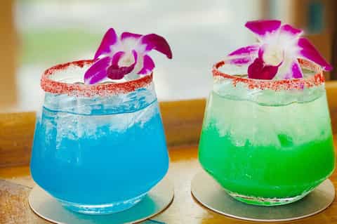 Two vibrant cocktails with sugar-rimmed glasses and orchid flowers at a resort bar.