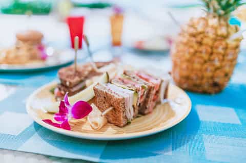 Tropical beach picnic spread with sandwiches, pineapple, and colorful drinks