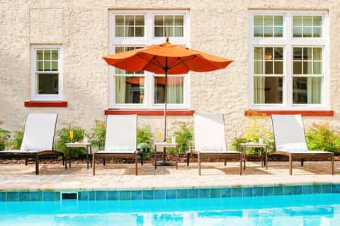 Poolside lounge chairs with orange umbrella against cream stone building facade